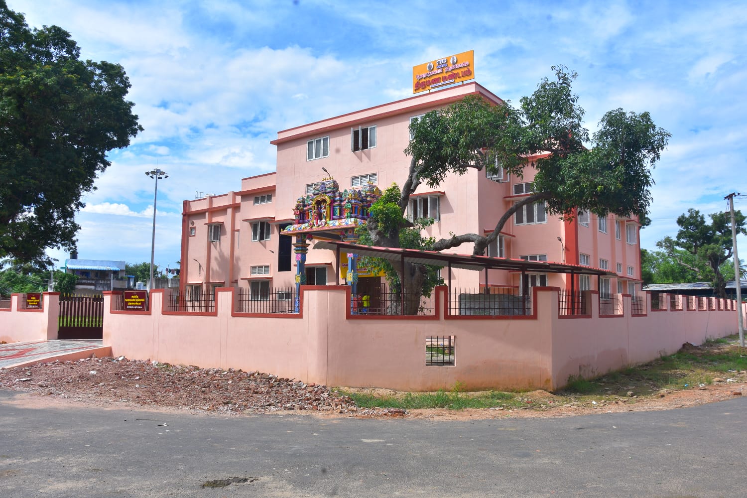 Three-storey kalyana mandapam corner view with compound wall and landscaped surrounds